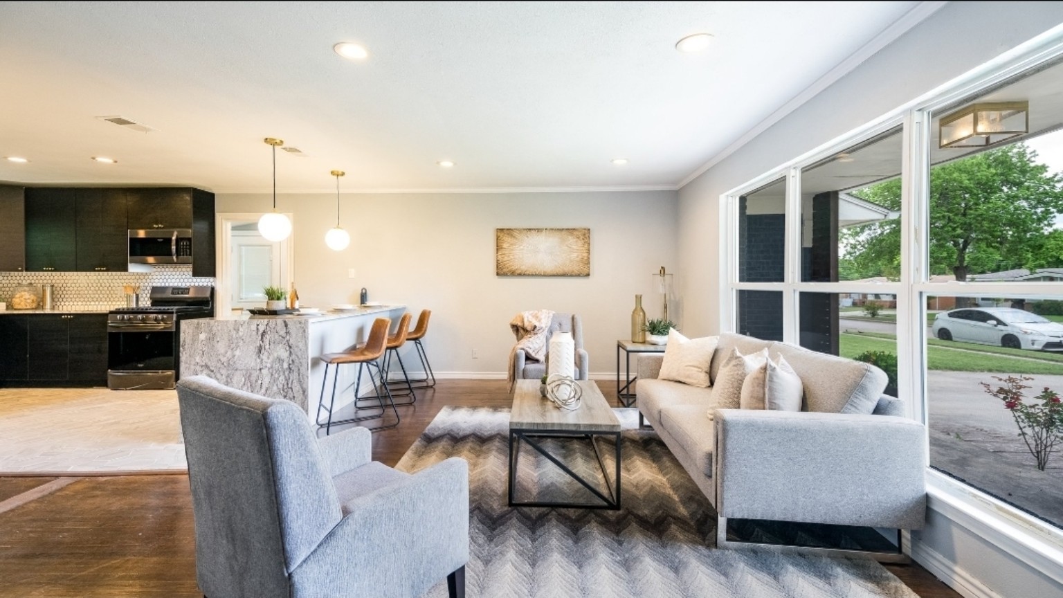 After: a bright living area with pale walls, large windows, staged seating and an open kitchen.